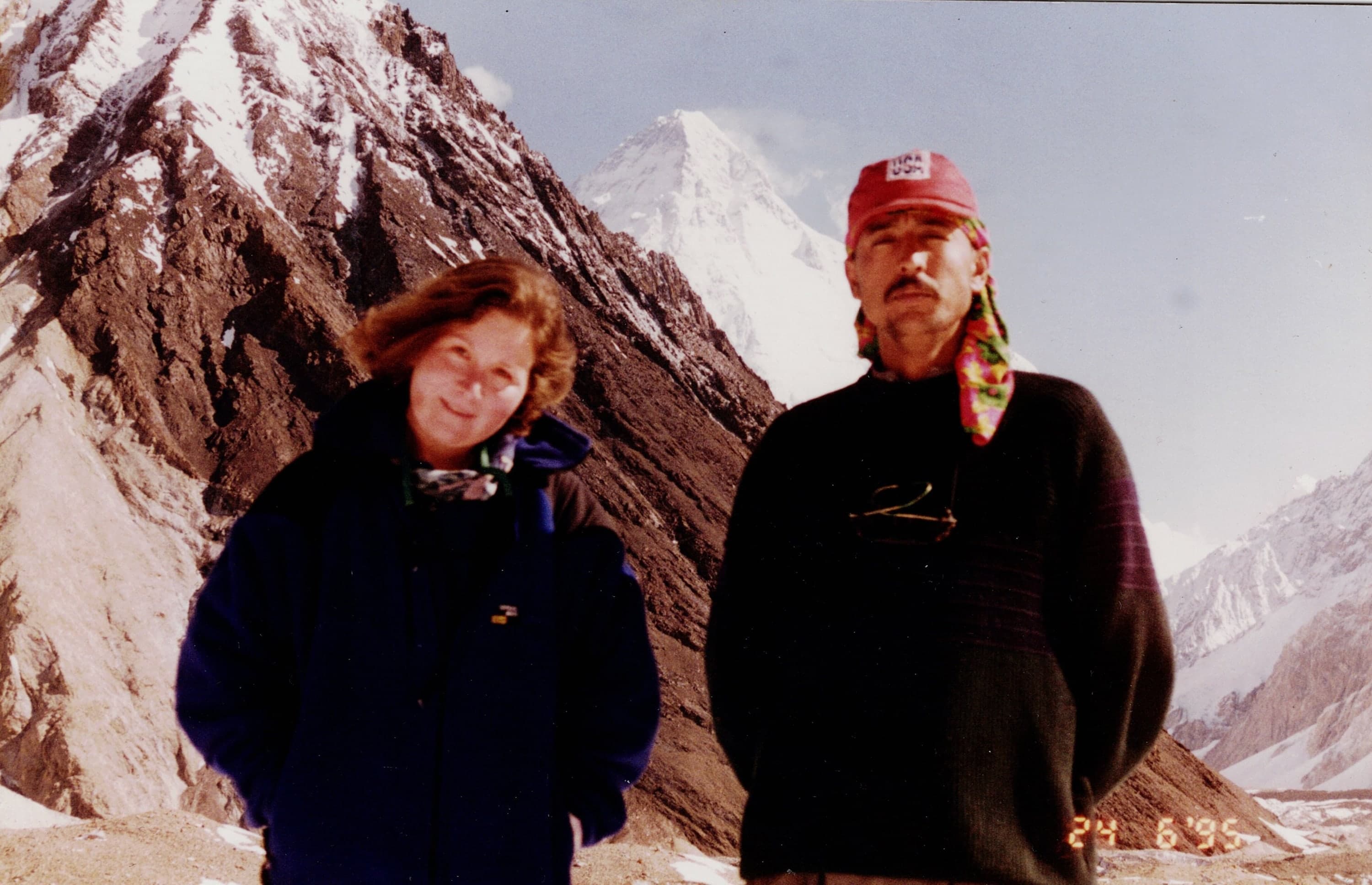 A woman and a man in a red cap on the Baltoro Glacier with K2 behind, June 1995