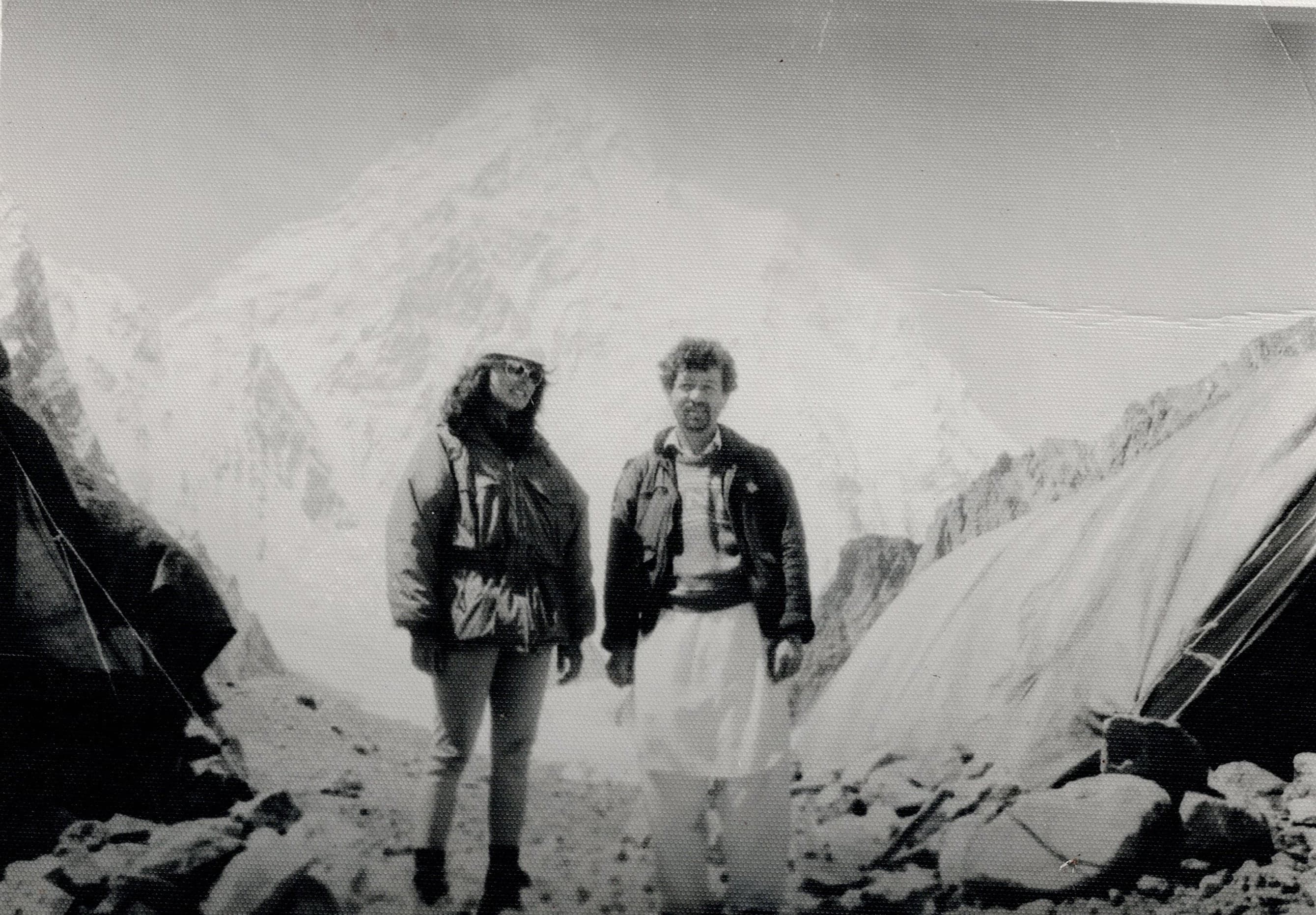 Black and white photo of two travellers outside a tent below a hazy Karakoram peak