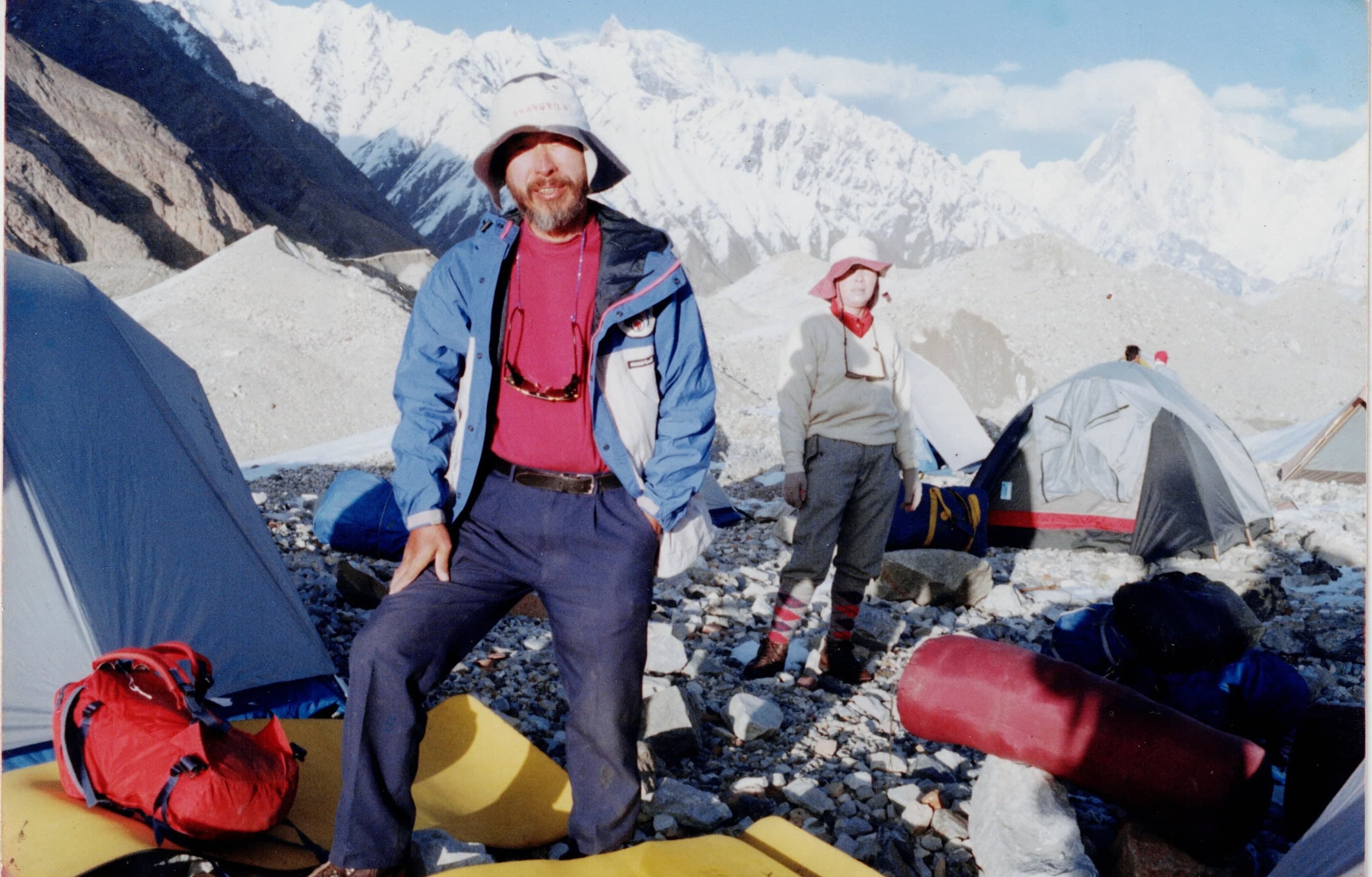 Tents pitched on rocky glacier moraine with snow peaks behind, Karakoram expedition camp