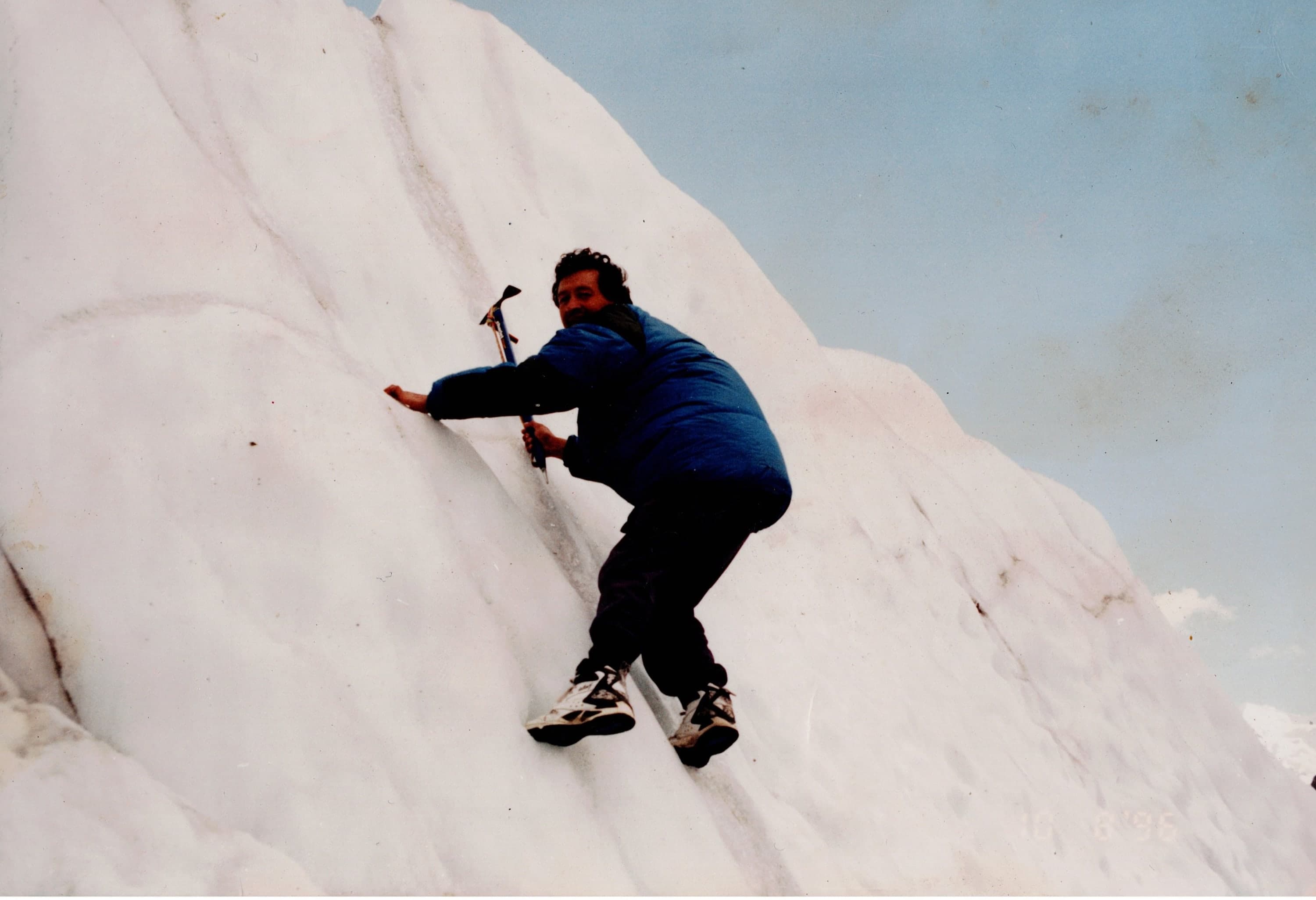 A man climbing a steep glacier ice wall with an ice axe