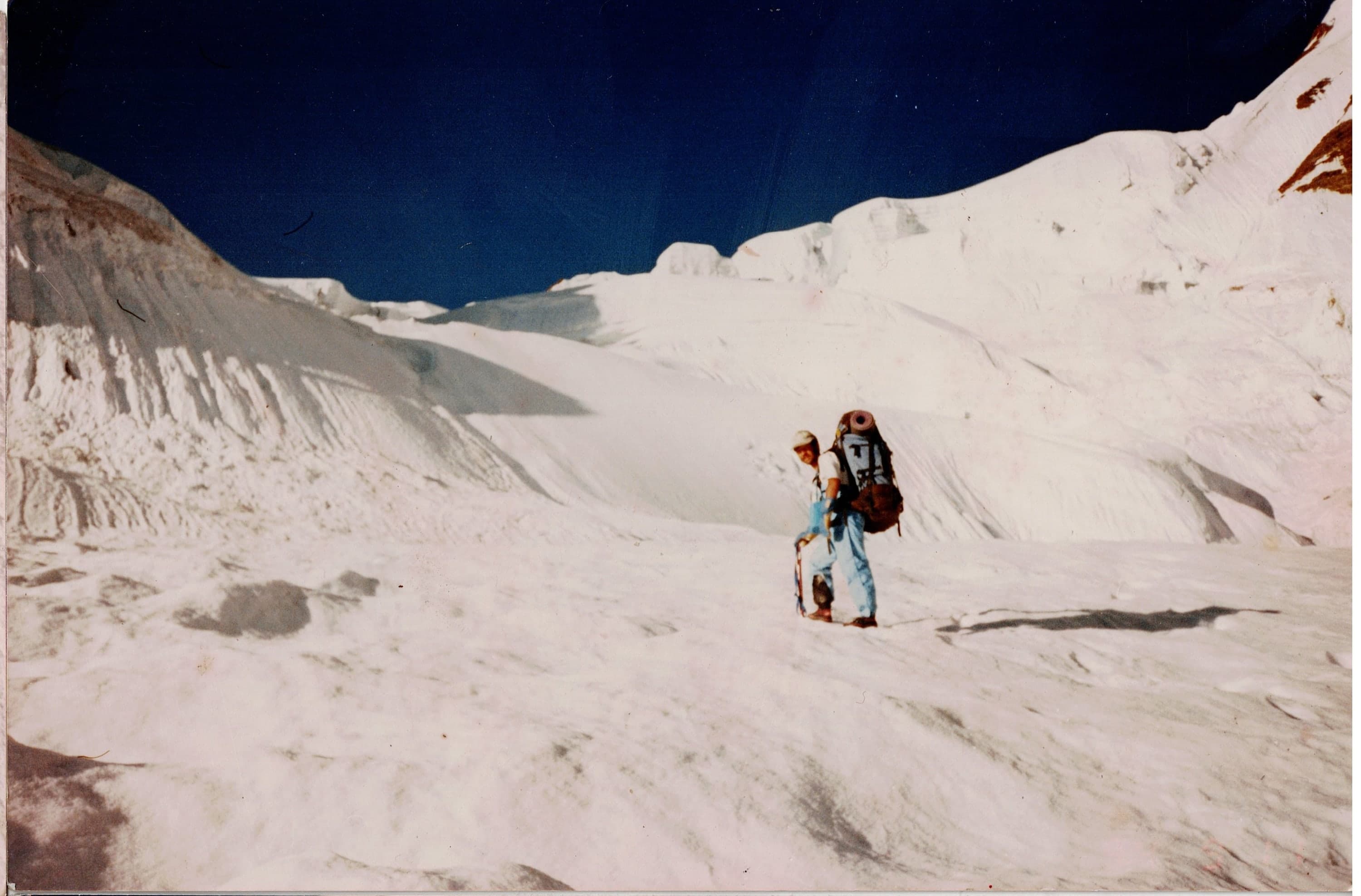 A climber with a heavy pack crossing a wide high-altitude snowfield