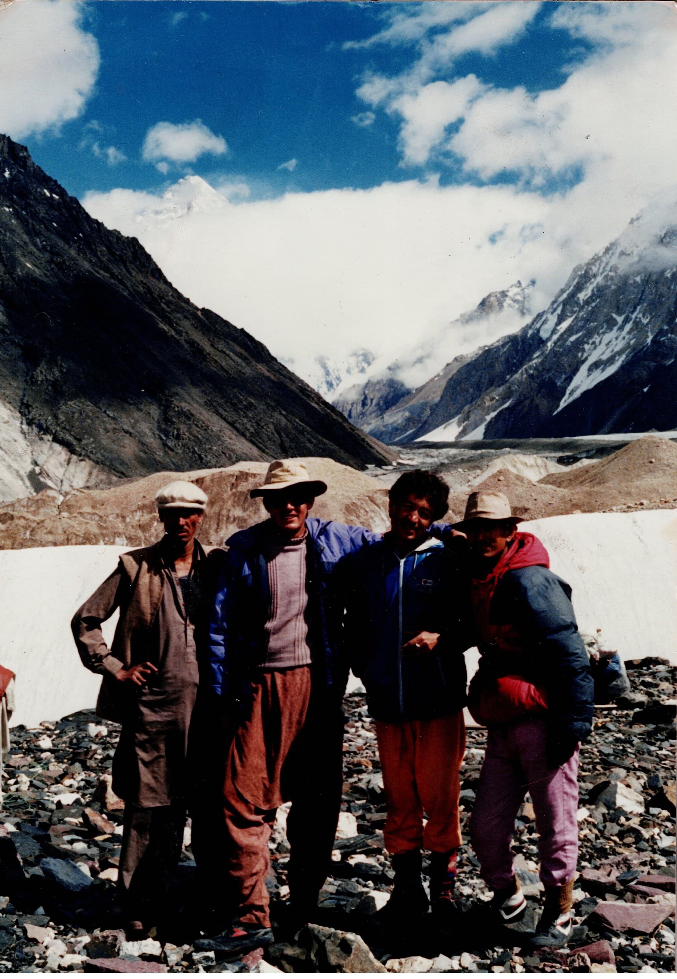 Four men standing together on rocky glacier moraine with cloud over Karakoram peaks
