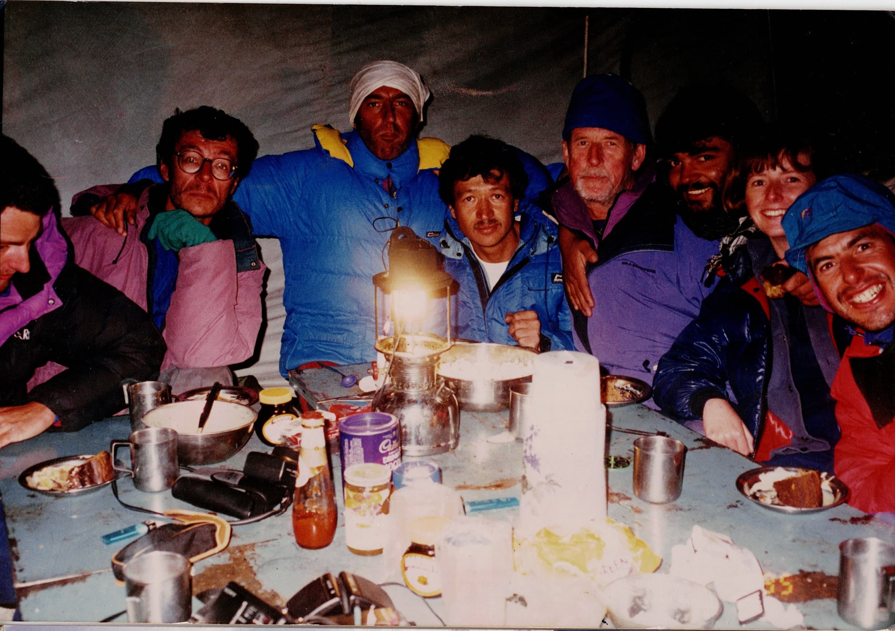 Expedition crew and foreign climbers sharing dinner by lantern light in a mess tent