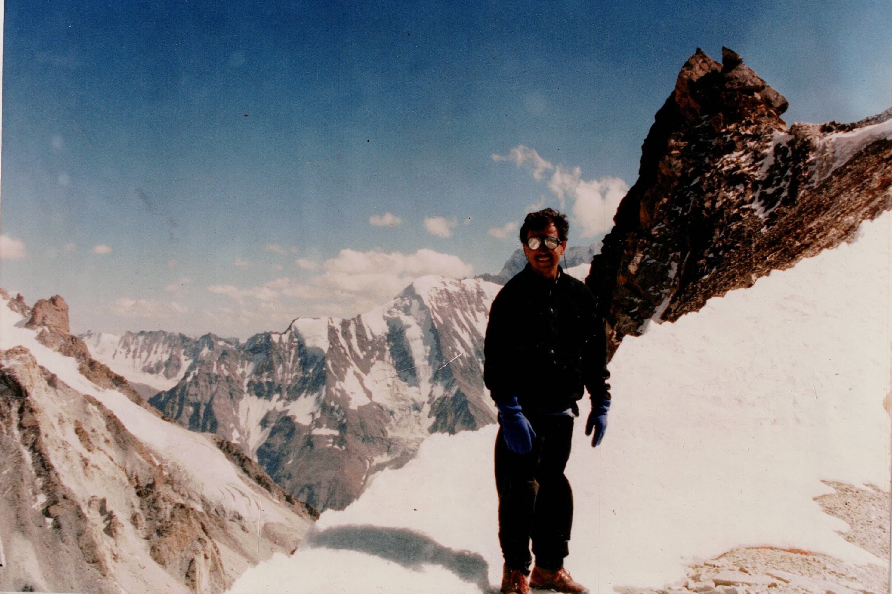 A man standing on a snow ridge with rock towers and Karakoram glaciers behind