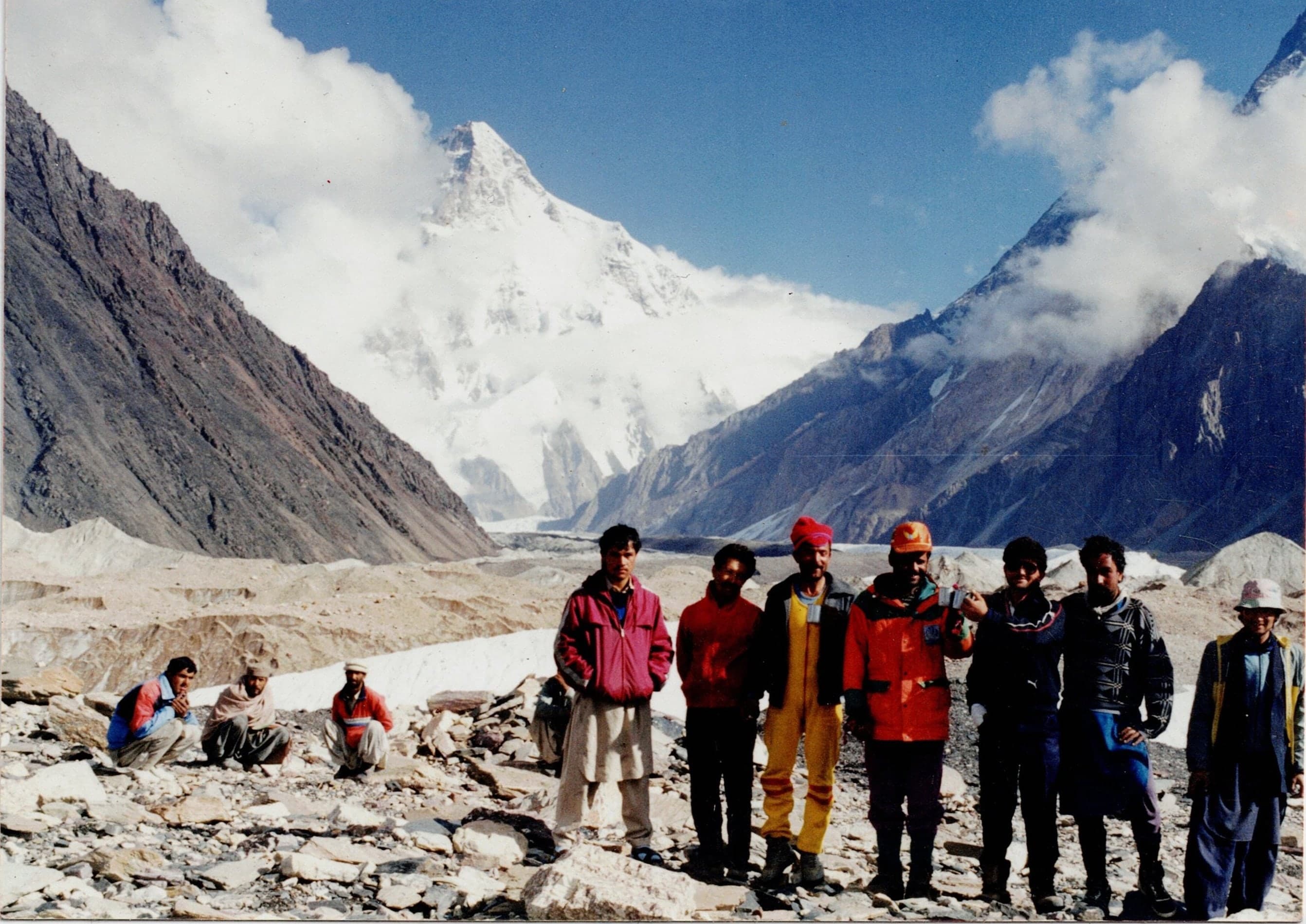 Porters and expedition crew standing on glacier moraine with K2 behind them