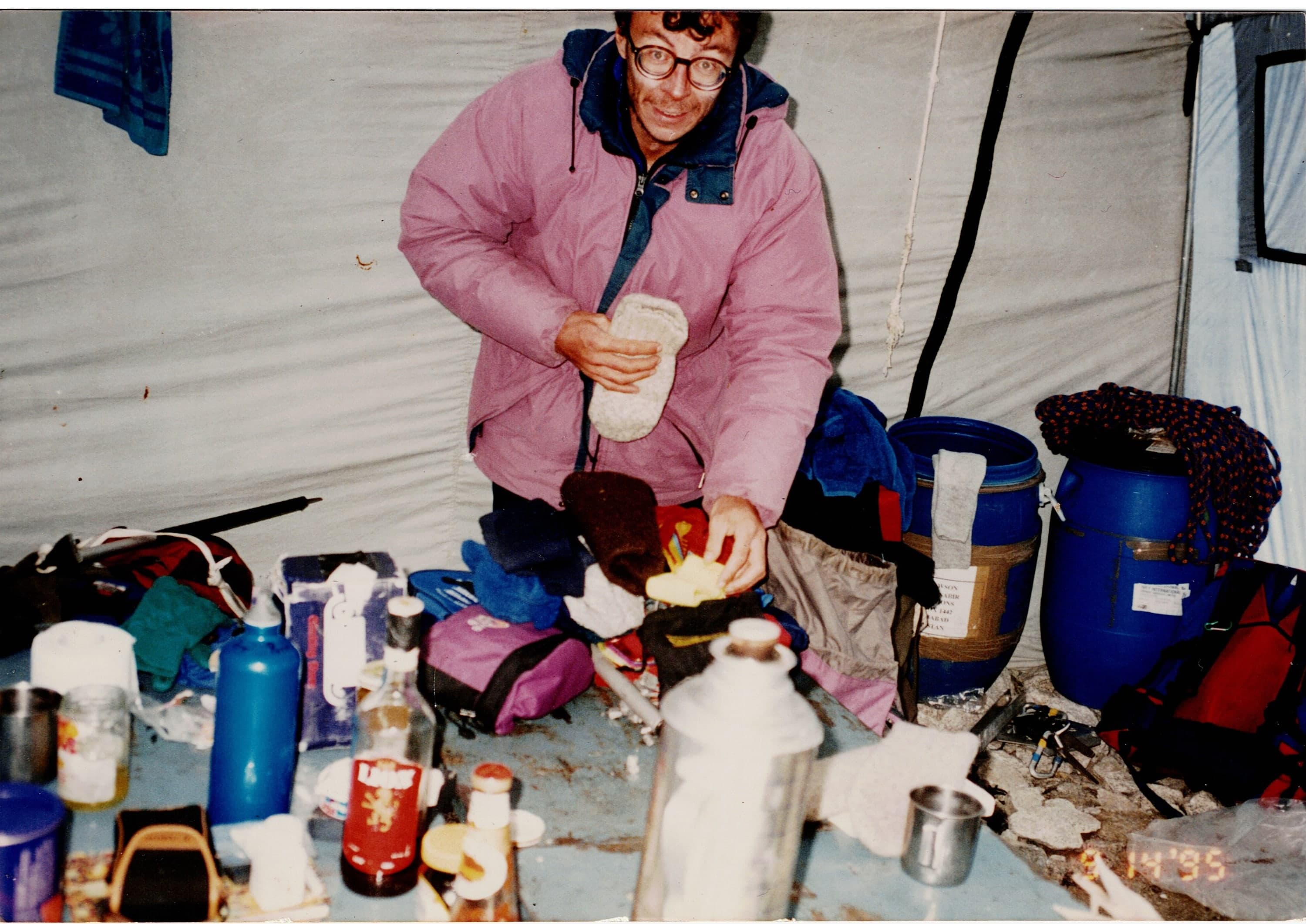 A man in a pink down jacket sorting expedition supplies inside a store tent, 1995