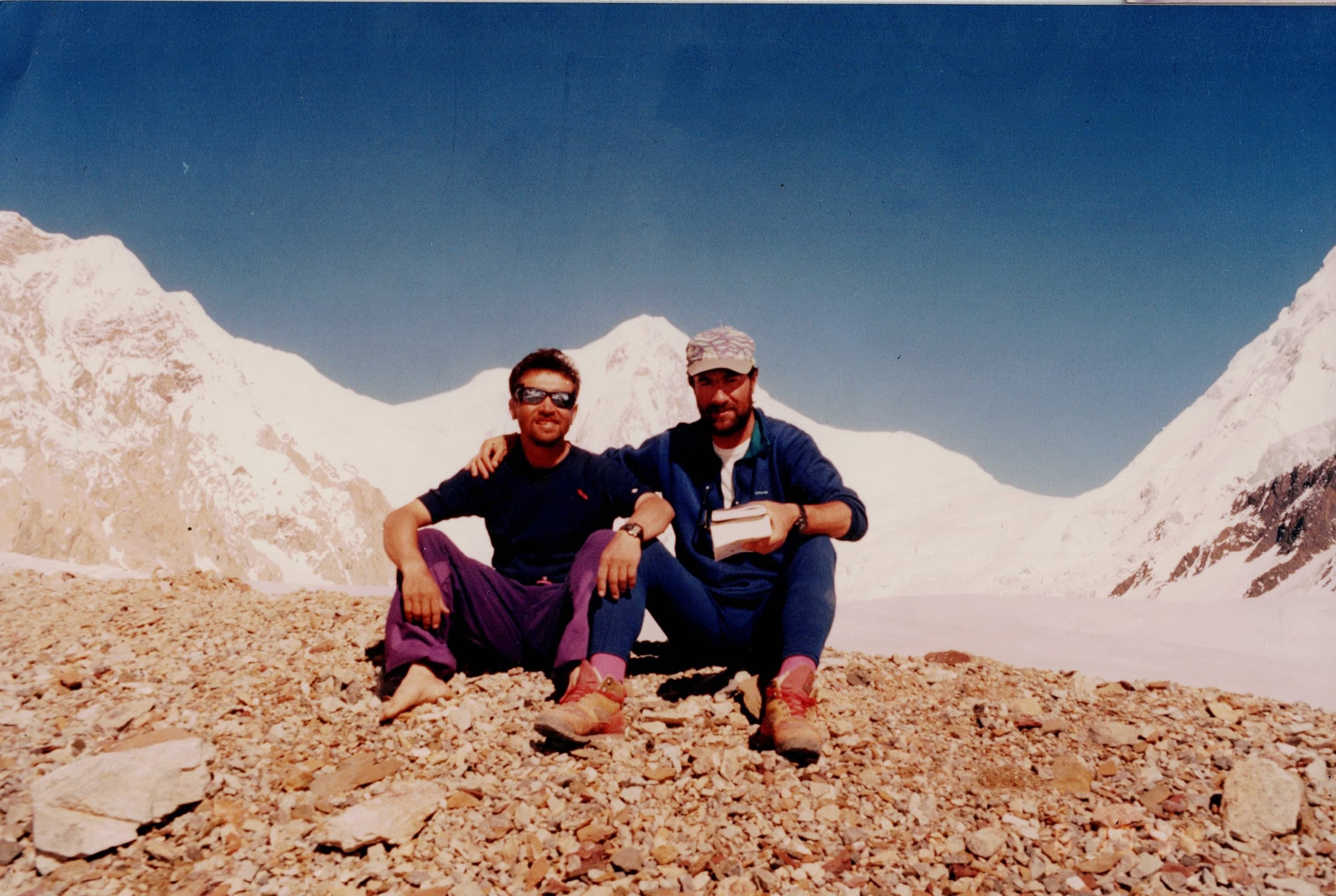 Two men sitting together on glacier moraine with a snow peak behind