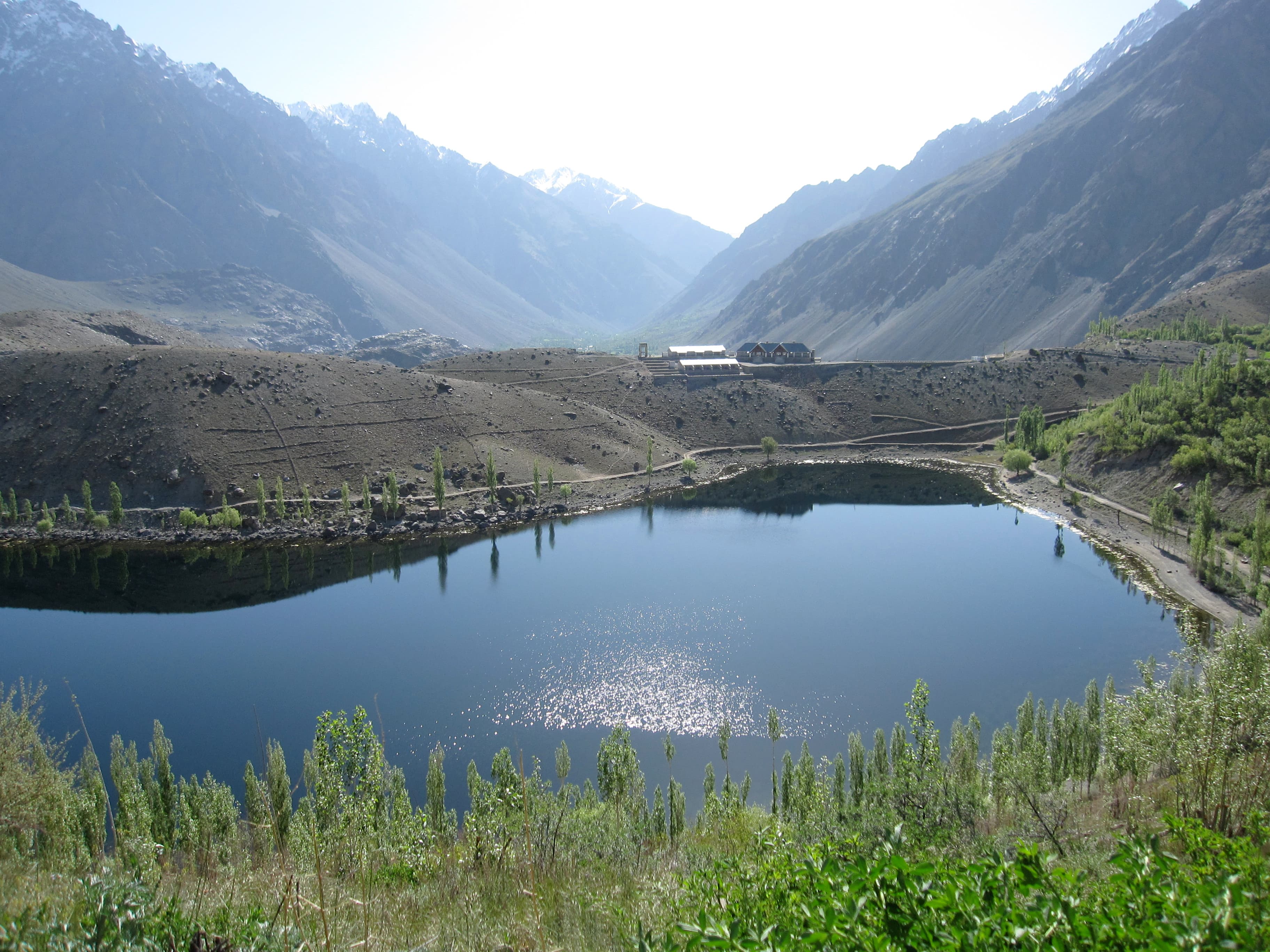 Deep-blue water of Phander Lake surrounded by green fields and poplar trees